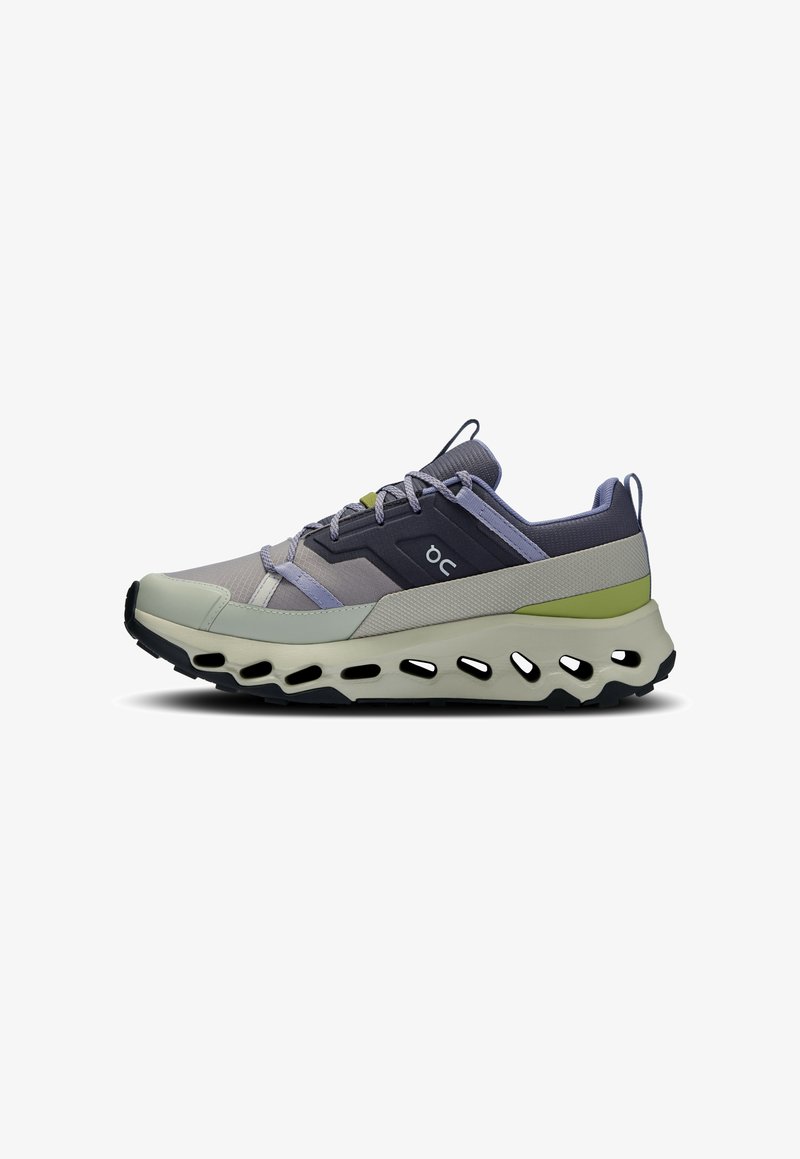 Chaussure de sport basse avec des accents gris, noirs et verts, tige en mesh respirant, fermeture à lacets et semelle épaisse avec des trous de ventilation découpés.