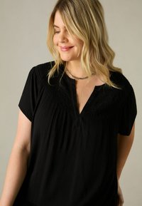 Svart kortärmad topp med en strukturerad design, med en v-ringning och rynkdetaljer vid axelområdet.