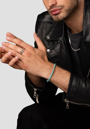 Black leather jacket, silver zipper details, silver ring, and a turquoise beaded bracelet on a hand with visible skin texture.