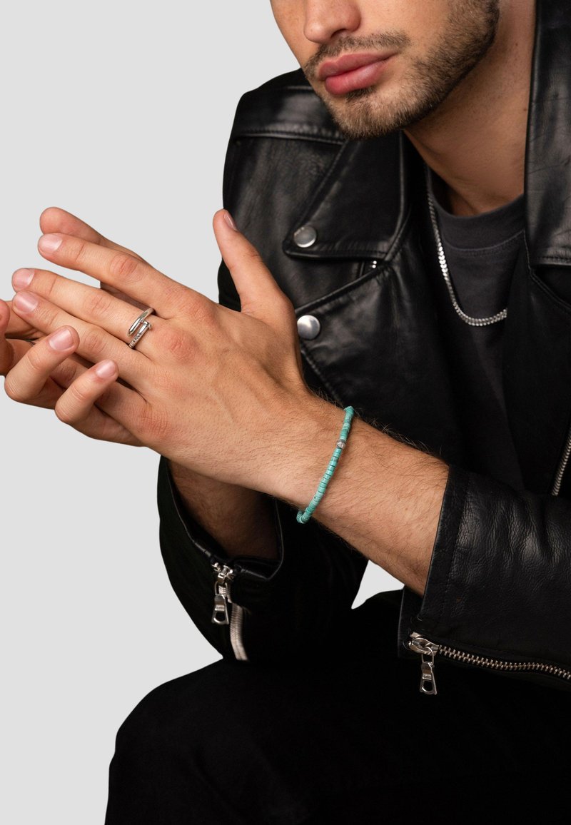 Black leather jacket, silver zipper details, silver ring, and a turquoise beaded bracelet on a hand with visible skin texture.