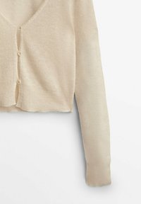 Cardigan court beige en maille avec manches longues et petits boutons devant sur un fond blanc uni.