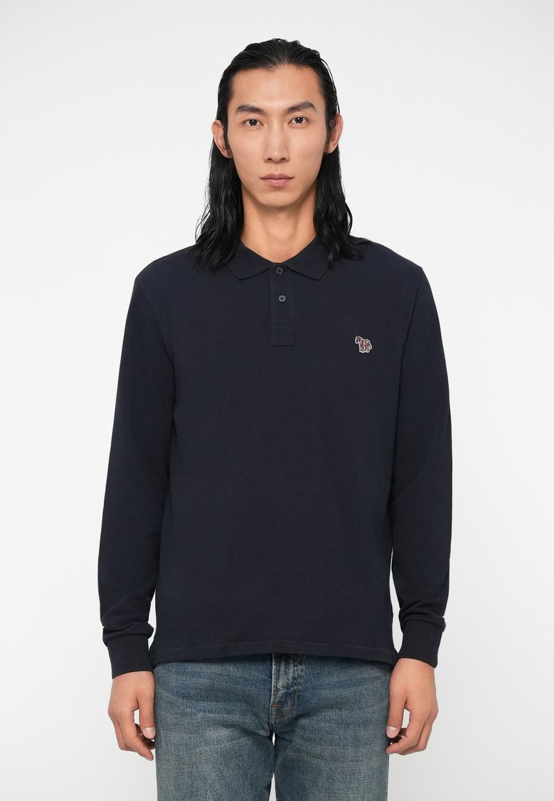 Camisa polo de manga longa em algodão na cor azul-marinho, com colarinho clássico, parte frontal com botões e bordado colorido de um elefante no lado esquerdo do peito.