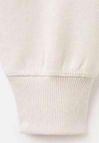 Poignet de sweat-shirt beige clair avec des détails côtelés texturés. Tissu doux avec une finition lisse, présentant un design uni et des coutures. 