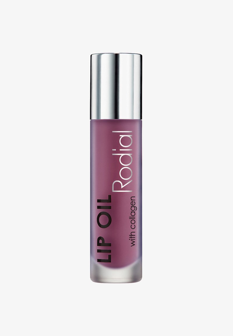 Lippenöl in einer klaren, zylindrischen Glasflasche. Die Flüssigkeit ist ein sanftes Lila. Silberne Metallkappe; schwarze Schrift mit Marken- und Produktdetails.