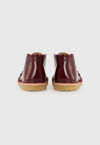 Bottines en cuir verni bourgogne avec bords festonnés, semelle en caoutchouc beige et texture lisse. La vue arrière montre une couture le long de la semelle.