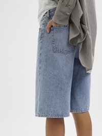 Calças de ganga azul claro, com corte reto, de comprimento médio, e um design clássico de cinco bolsos; combinadas com uma camisa xadrez preta e branca.