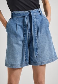 Ljusblå denimshorts med bälte i midjan, veckad front och sidofickor. Avslutade med en rullad fåll och kontraststygning.