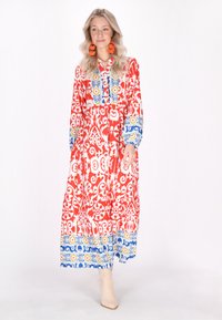 Rochie lungă roșie cu modele intricate albe, accente albastre și galbene la guler și mâneci, cu o fustă fluidă și mâneci lungi.