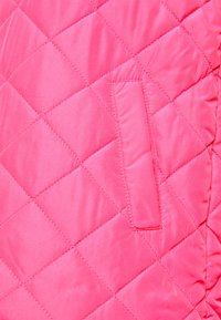 Tecido acolchoado rosa com um padrão de diamante, apresentando um pequeno bolso costurado no lado esquerdo, textura suave com acabamento brilhante.