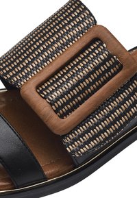 Svart och tan sandal med ett brett vävt band och en träspänne, slät läderbas och en texturerad innersula för komfort.