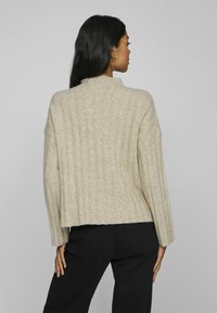 Beige geribbelde gebreide trui met een hoge hals en verlaagde schouders, met een cropped zoom en een zachte textuur. Draag gecombineerd met zwarte broek.