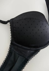 Black padded bra with polka dot pattern, lace trim along the edges, and thin adjustable straps, featuring a smooth satin-like texture.