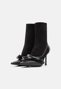 Bocanci negri până la glezne, din suede și piele, cu vârf ascuțit, toc stiletto și o fundă decorativă în față.