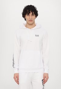 Hvid hoodie med snoretræk, kængurulomme og sort logo på brystet. Lange ærmer har sort tekstdesign. Blødt, glat stof.