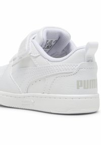 Bijela tenisica s teksturiranim kožnim gornjim dijelom, čičak trakom, podstavljenim ovratnikom i izgleda posebno s Puma logom u svijetlosivoj boji na peti.