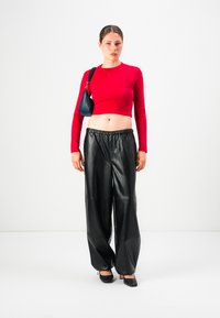 Young woman wearing a red long-sleeve cropped top, black wide-leg leather pants, black heels, and carrying a small black shoulder bag.