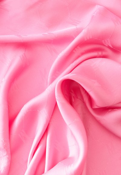 Tissu rose lisse et brillant avec des motifs subtils, doucement plié et froncé avec des reflets de lumière visibles à sa surface.