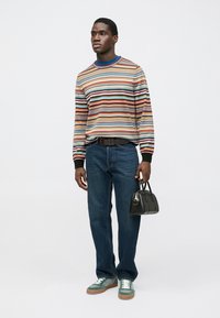 Striped knit sweater in various colors, dark jeans, green sneakers, and a small black handbag with a top handle.