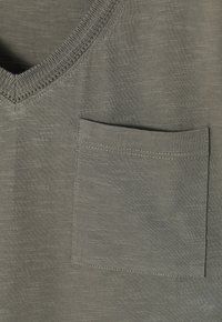 Tissu tricoté vert olive avec un col en V et une poche carrée cousue sur le côté droit de la poitrine.