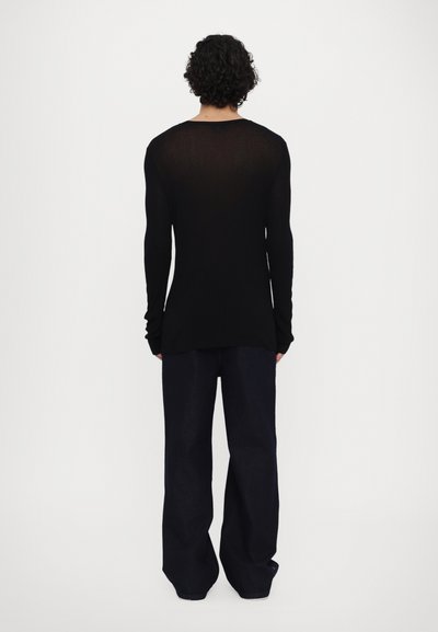 Haut noir à manches longues en tissu léger et texturé. Design ajusté avec un col rond et des manches ajustées, associé à un pantalon sombre.