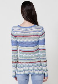 Multifarvet strikket sweater med horisontale striber i blå, grøn, rød og hvid, med en tekstureret, åben vævning og bølget kant.