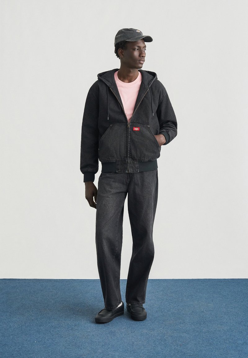 Zwarte denim hoodie met een ritssluiting aan de voorkant en trekkoorden, gecombineerd met een lichtroze T-shirt en zwarte jeans, compleet met zwarte schoenen.