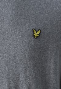 Maglione grigio lavorato a maglia con una finitura testurizzata e un logo aquila ricamato giallo e nero sul lato sinistro del petto.