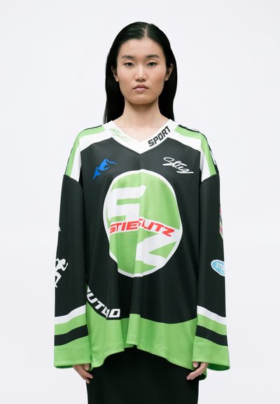 Sort og grøn oversized sports trøje med V-hals. Har logoer og grafik, herunder 'STIELITZ' i rød på fronten.