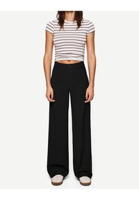 Svarta vida byxor med en slät textur, med framknäppning och bältesöglor, kombinerade med en figurnära randig crop top.