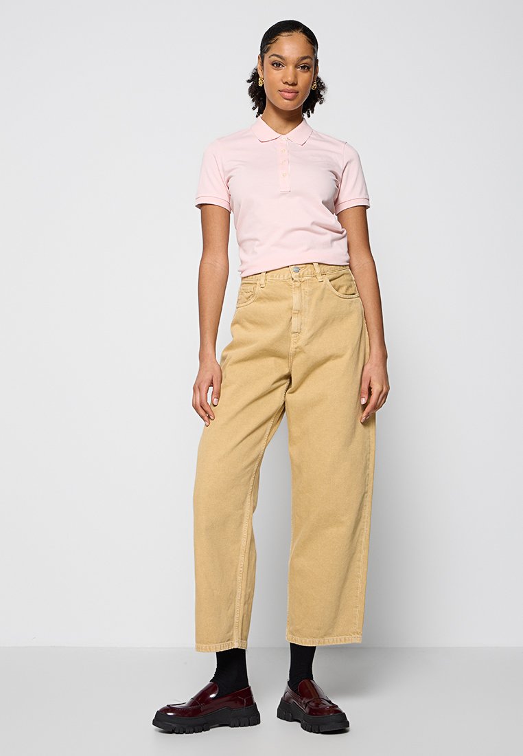 Polo rose avec un col, accompagné d'un pantalon beige ample. Des chaussettes noires à la cheville et des chaussures bordeaux brillantes complètent la tenue.