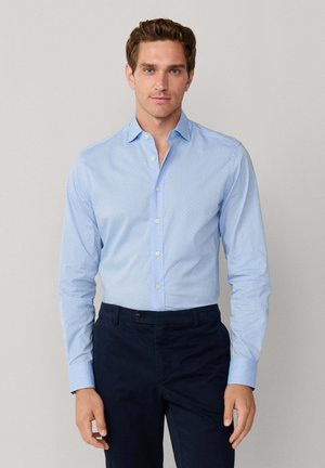 Lichtblauw overhemd met knopen met kleine witte stippen, lange mouwen en een klassieke kraag, gecombineerd met marineblauwe broek.