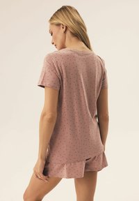 Krótki zestaw nocnej odzieży z krótkim rękawem w miękkim różowym materiale, z czarnymi kropkami; zawiera koszulę z okrągłym dekoltem oraz pasujące szorty.