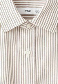 Bílá košile s tenkými hnědými pruhy, s klasickým límečkem a zapínáním na knoflíky. Vyrobena z hladké látky s jemným leskem.