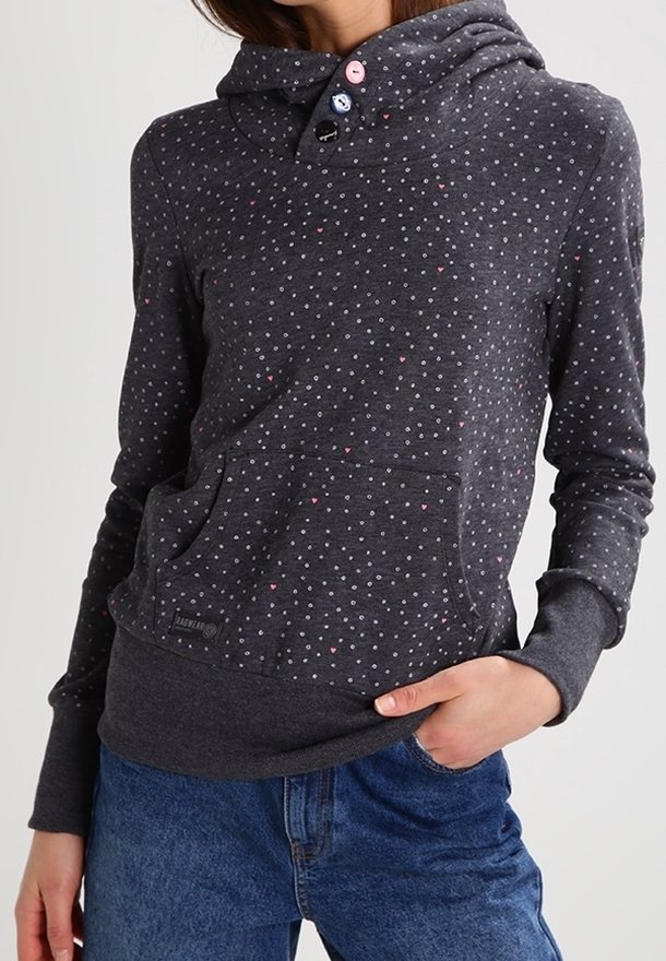 Felpa grigia scura con piccoli pois bianchi e rosa, tre bottoni sul colletto, tasca a marsupio, indossata con jeans blu.