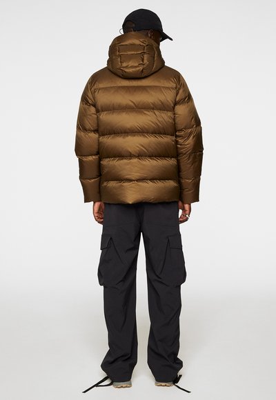 Brun puffjacka med horisontella kanaler och huva, kombinerad med svarta cargo-byxor. Jackan har en slät yta och en praktisk design.