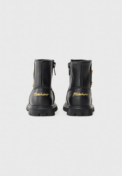 Botines negros de cuero con cierre de cremallera, suela de goma y logo bordado en dorado en el talón, que presentan un diseño elegante y resistente.