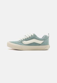 Light blue suede sneaker with white accents, laces, and a textured finish. Features a rounded toe and a simple, low-profile design.