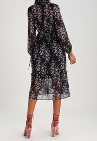 Musta kukallinen midi-mekko pitkillä hihoilla, kootulla vyötäröllä ja röyhelöhelmalla. Läpinäkyvä kangas, jossa on värikkäitä kukkakuoseja. Vaaleanpunaiset nilkkurit.