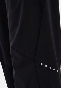 Black athletic pants made of a smooth, stretchable fabric. Features a sleek design with a diagonal seam and five small reflective dots.