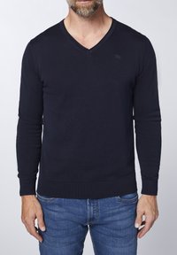 Marinblå v-ringad tröja i ribbad stickning, med långa ärmar och en åtsittande nederdel. Litet logotypaccent på bröstet.