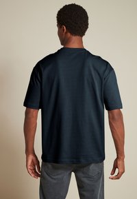 Mørkeblå kortærmet T-shirt lavet af glat stof, med en klassisk rund halsudskæring og afslappet pasform, båret med grå jeans.