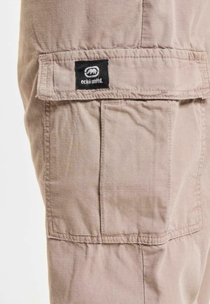 Beige cargo pants with a textured fabric, featuring a prominent flap pocket and a black Ecko Unlimited logo tag on the front.