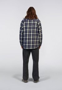 Camicia di flanella a scacchi in blu navy e crema, design con bottoni, dal fitting comodo; abbinata a pantaloni grigio scuro e stivali robusti.
