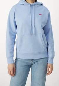 Světle modrá mikina s kapucí, přední kapsou, stahovací šňůrkou, žebrovanými manžetami a malou červenou nášivkou logo Levi's na hrudi.