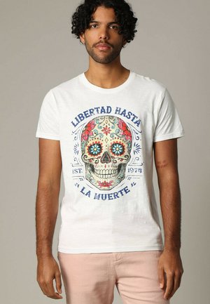 T-shirt blanc avec un design coloré de crâne sucré, orné de motifs floraux et du texte "Libertad Hasta La Muerte" en bleu, style col rond.