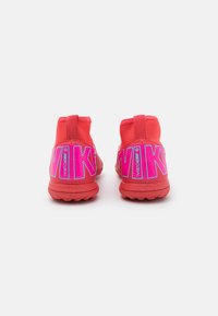 Red athletic shoes featuring a high-top design, smooth texture, prominent pink branding, and a flexible outsole.