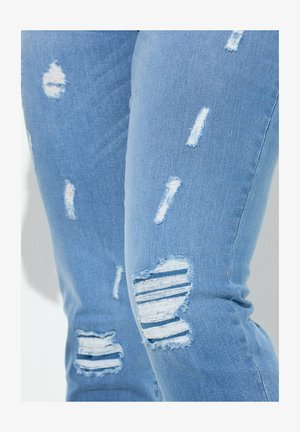 Jeans azzurri strappati in denim, con diverse toppe usurate, inclusa una toppa a righe orizzontali sul ginocchio.