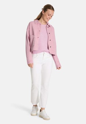 Hellrosa, kurz geschnittene Jacke mit Knopfverschluss und Brusttasche, getragen über einem hellrosa Pullover, kombiniert mit weißen Jeans und weißen Sneakers.