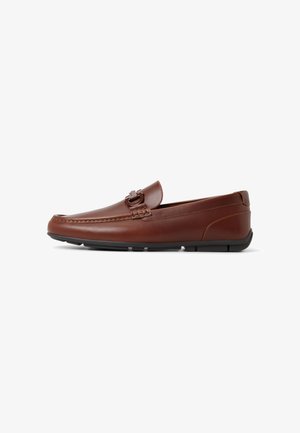 Mocasín de cuero marrón para hombre con suela de goma negra y detalle de hebilla metálica en la parte superior, mostrado de perfil lateral.