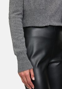 Pull en tricot gris avec un poignet côtelé, associé à un pantalon en cuir noir présentant une texture lisse et une coupe ajustée.